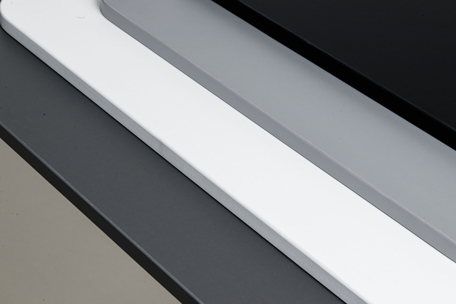 Black, grey and white Desko desktops stacked, showing rounded corners and eased edges